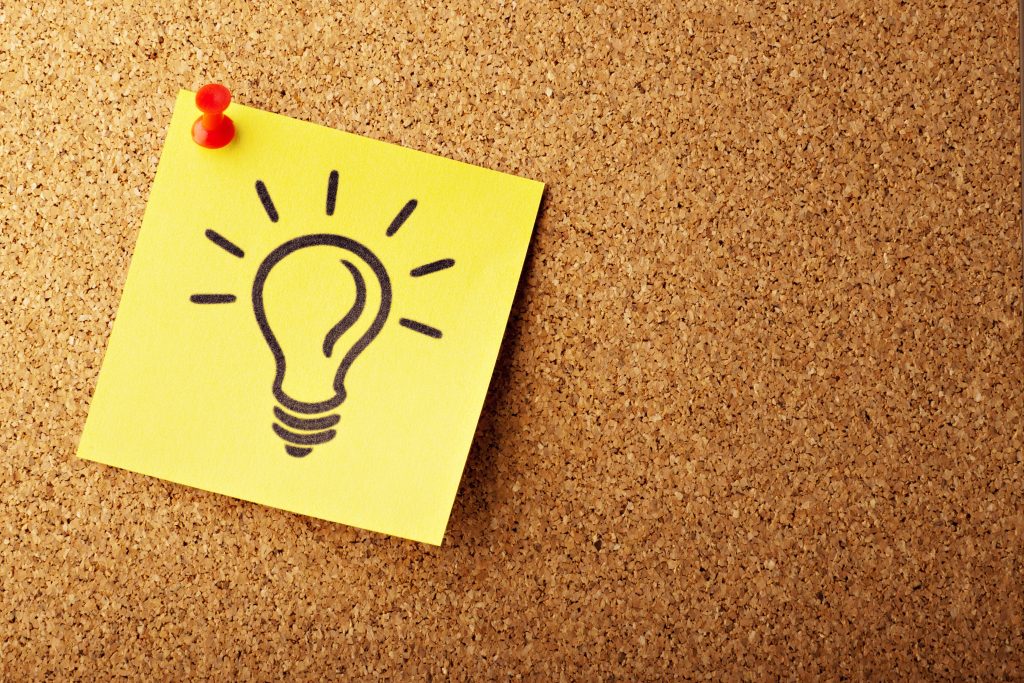 Yellow sticky note with light bulb on a cork board