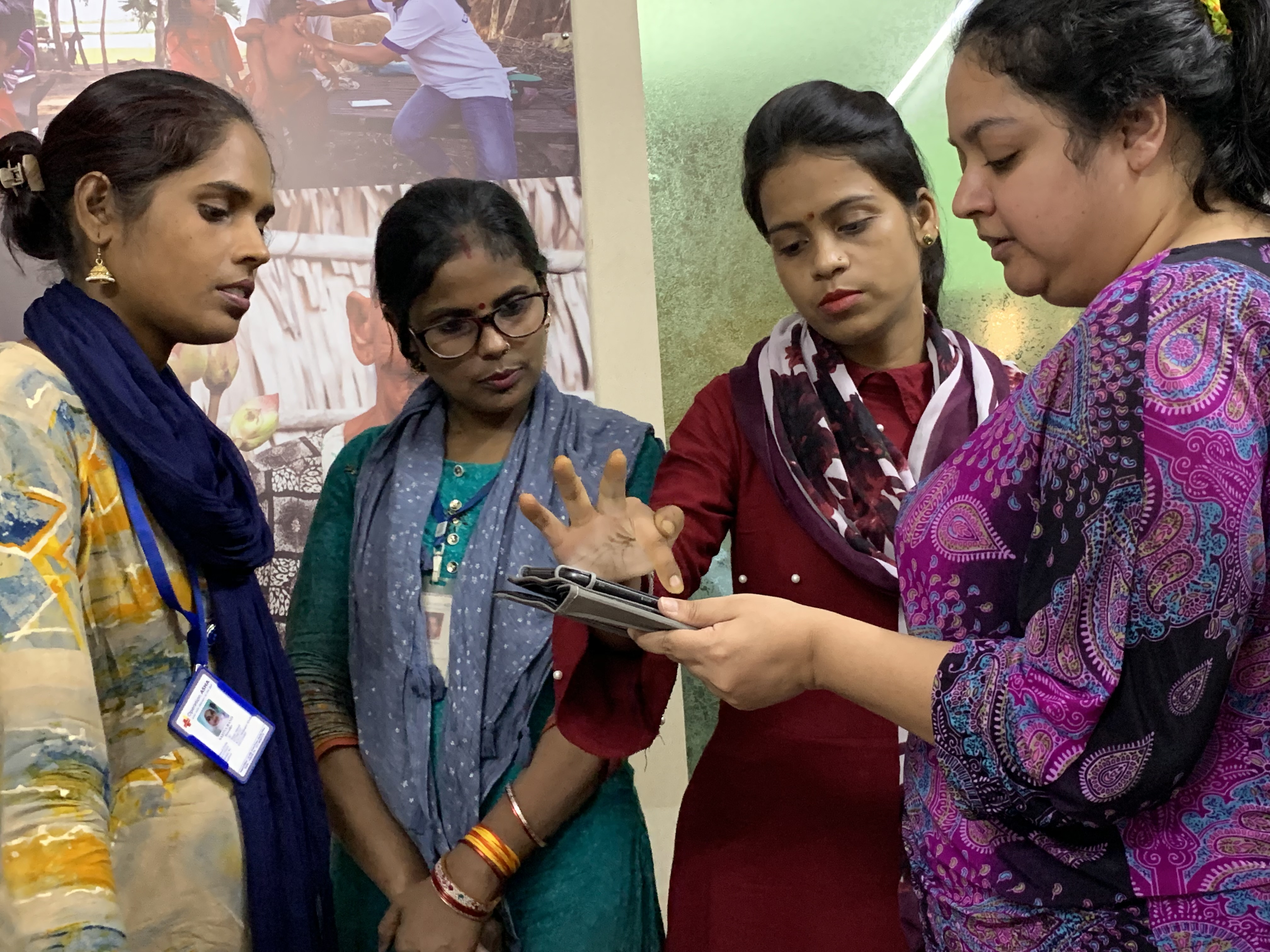 Four Operation ASHA employees looking at a tablet and pointing at and discussing different features