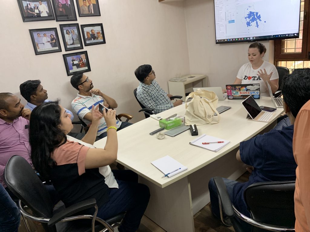 Tableau volunteer Lauren giving a demo of the Tableau software to Operation ASHA team members around a table who look on and take photos