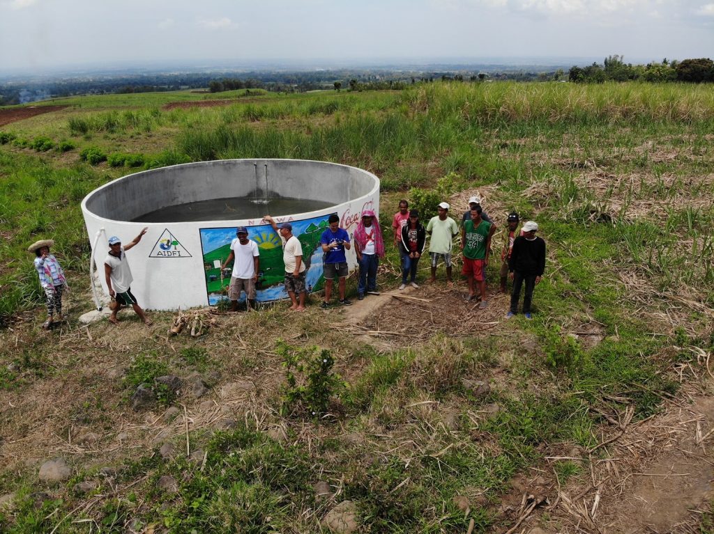 AIDFI team stands beside newly installed reservoir for Ram Pump to deliver water to village of Upper Atok